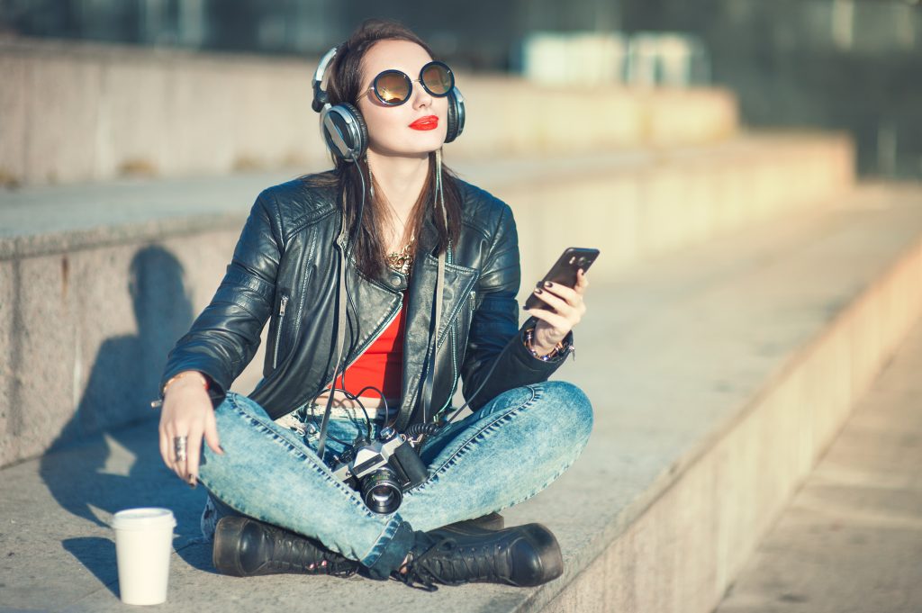 Hipster beautiful girl in leather jacket and glasses listening m