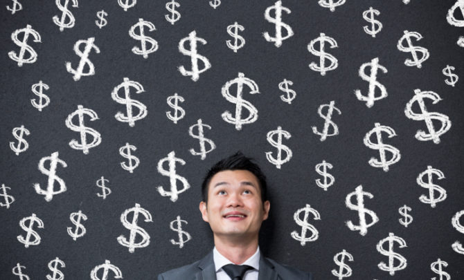 Chinese businessman in front of dollar signs written on wall.